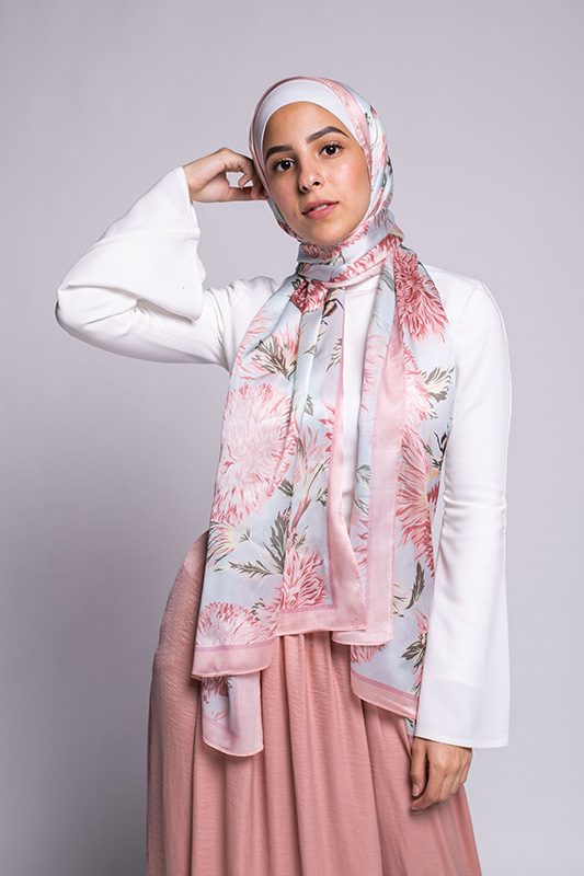 Hijabi Model in EMMA scarf Honey Blooms satin, a print of bees and delicate pink flowers with a pink border.looking at camera. hands on her neck