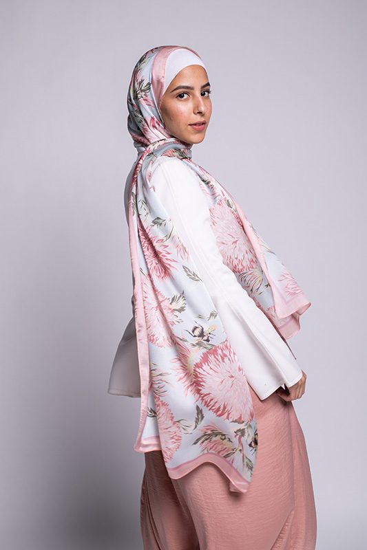 Hijabi Model in EMMA scarf Honey Blooms satin, a print of bees and delicate pink flowers with a pink border.turns around at camera