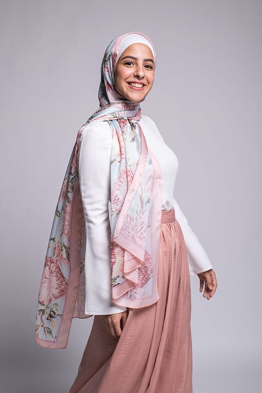 Hijabi Model in EMMA scarf Honey Blooms satin, a print of bees and delicate pink flowers with a pink border. Smiling