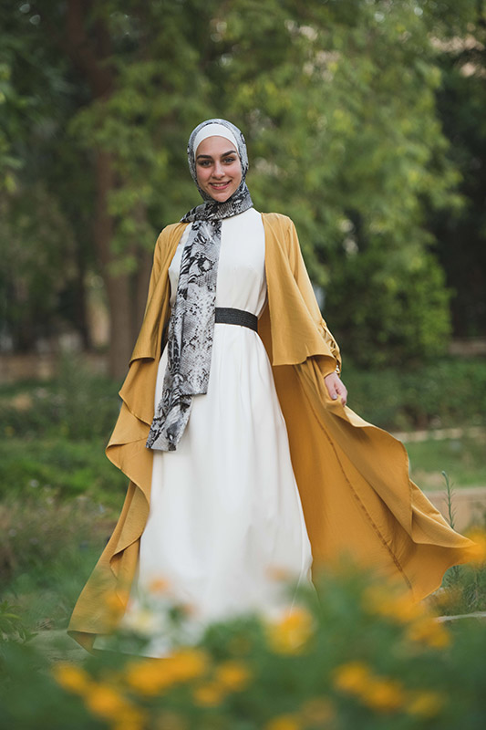 Hijabi Model EMMA Scarf Black Python smiling at camera in a white maxi dress and mustard kimono and a belt in a forest