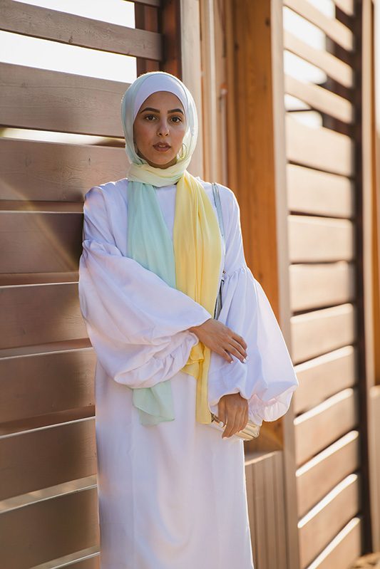 A hijabi Model in EMMA Scarf Kiwi Zest in a white frill sleeve dress holding her arm staring at a distance