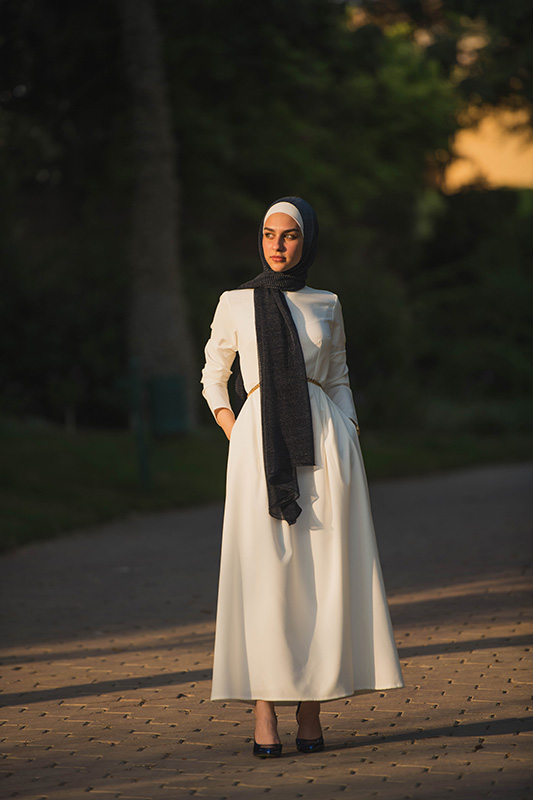 White hijabi model in EMMA Scarf Navy Shimmer staring at a distance in white maxi dress
