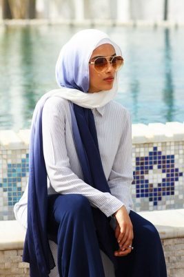 A hijabi model wearing EMMA scarf Frosted Coral in Ombre off white and blue by the pool