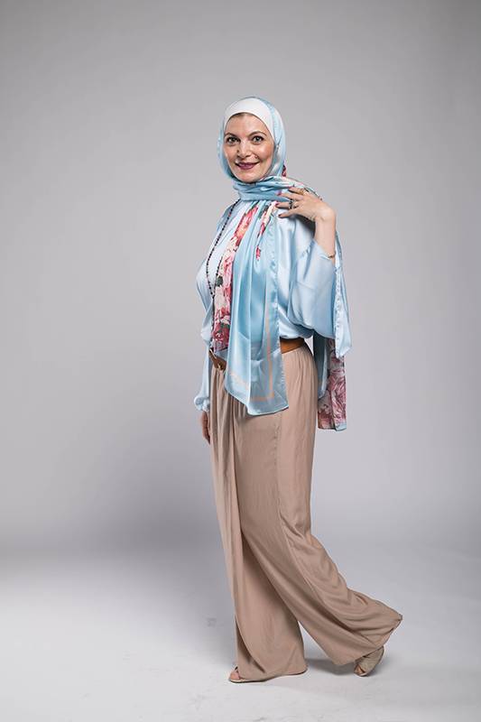 Hijabi Woman in EMMA scarf A close up f a hijabi woman in EMMA scarf Chains D'ior smiling and a baby blue satin top and brown pants