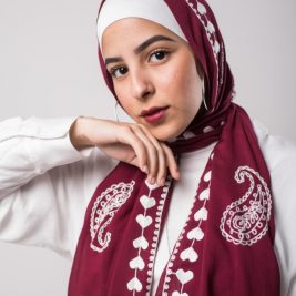 hijabi model in EMMA Scarf lOVE ME BURGUNDY in the color burgandy with plasely embroidered on it in off-white